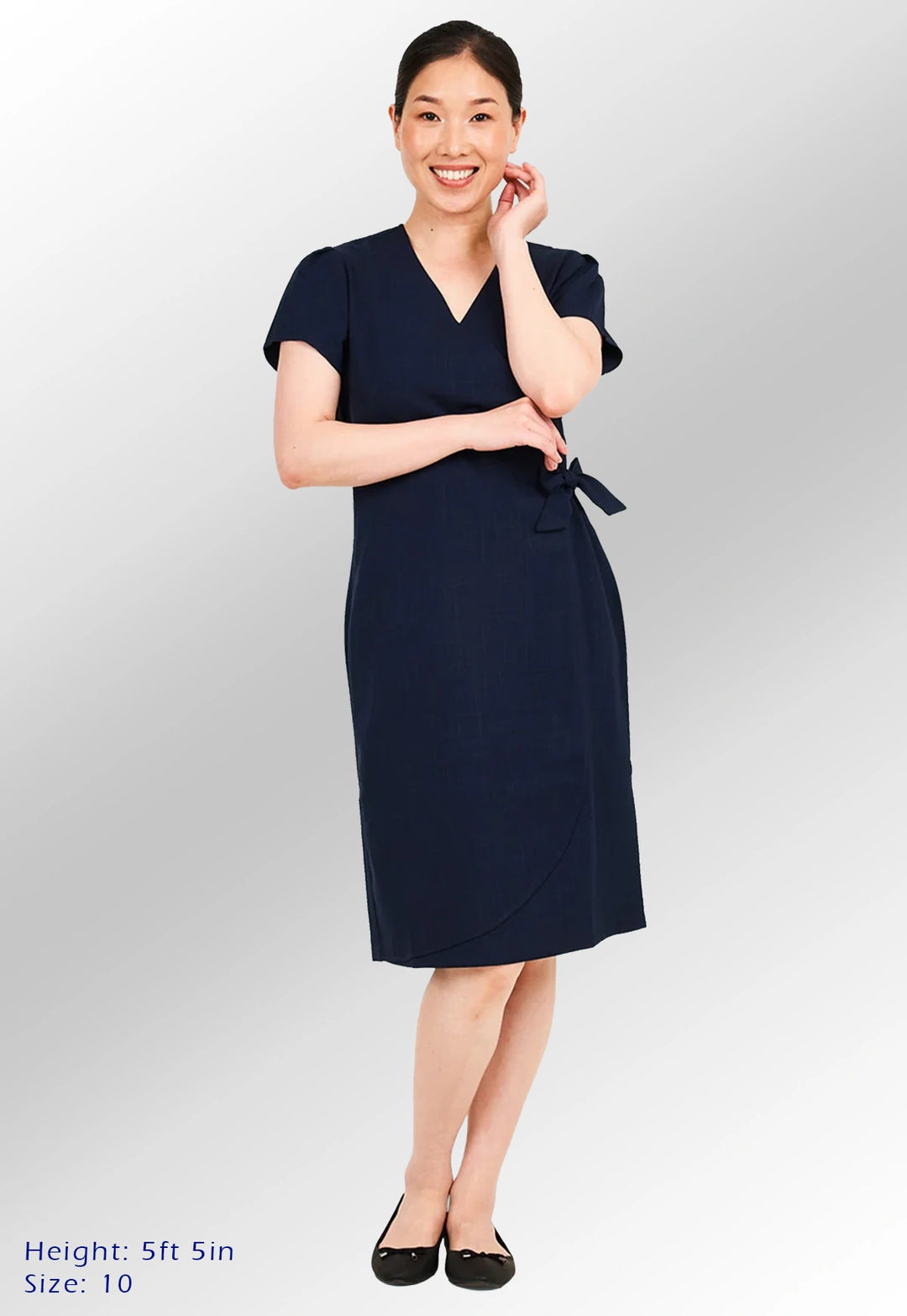 A woman modelling the Elena Wrap Over Salon Dress in Navy. Text in the lower left reads 'Height: 5ft 5in' and 'Size: 10'.