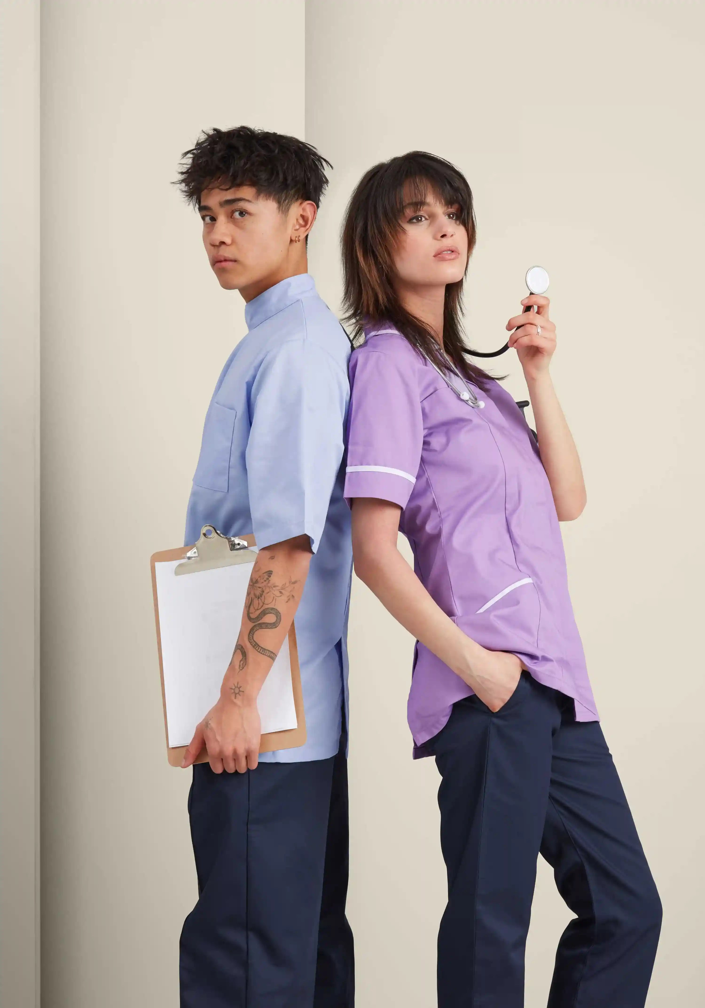 Two healthcare professionals in blue and purple scrubs against a plain background