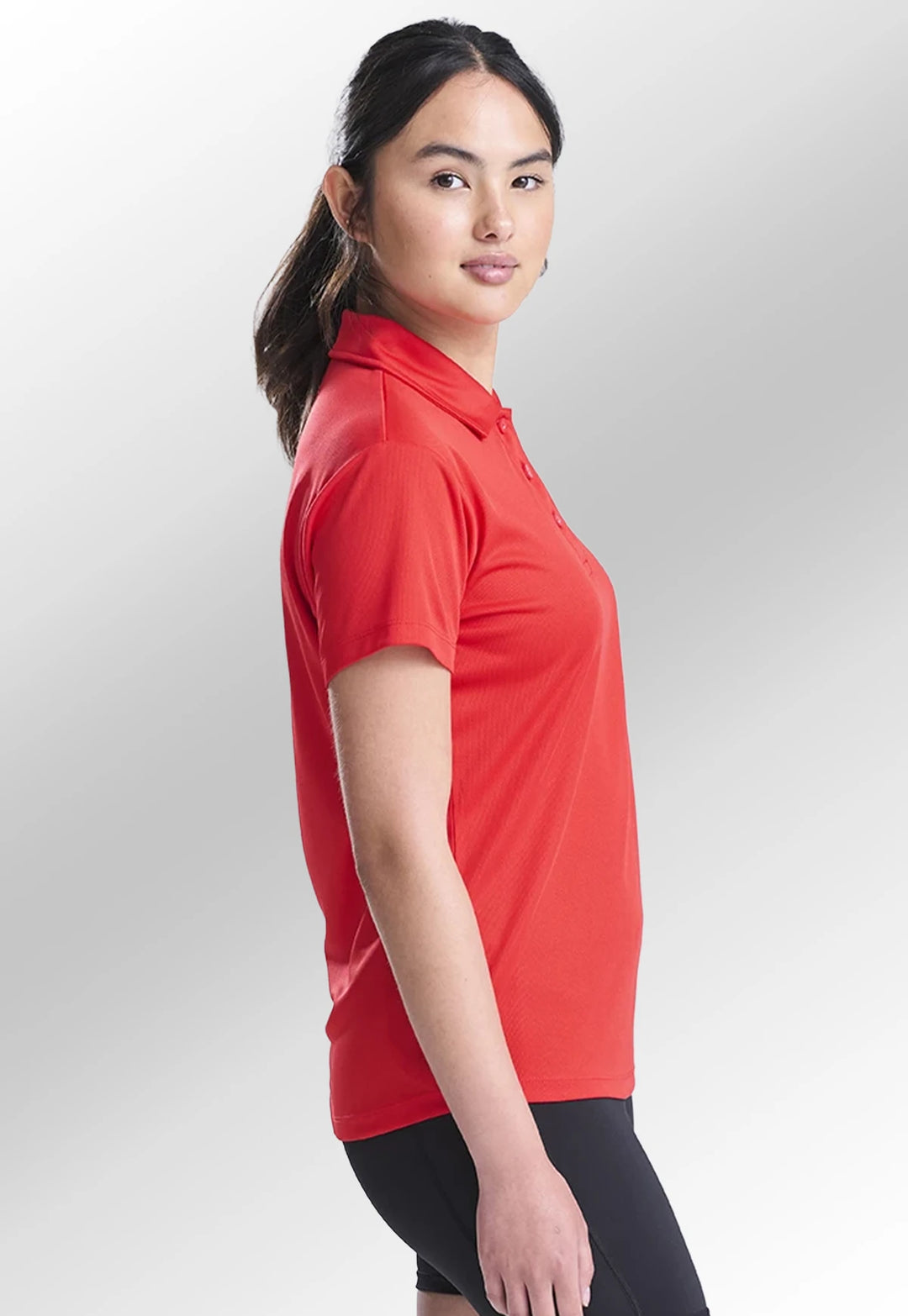 Side view of model wearing the AWDis Ladies Cool Polo JC045 in Fire Red.