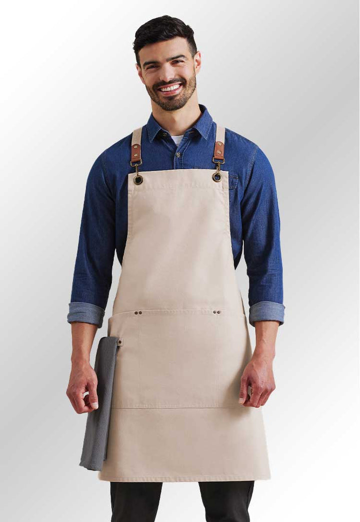 A model wearing a PR182 Clip ‘n’ Clasp cross-back bib apron in Natural