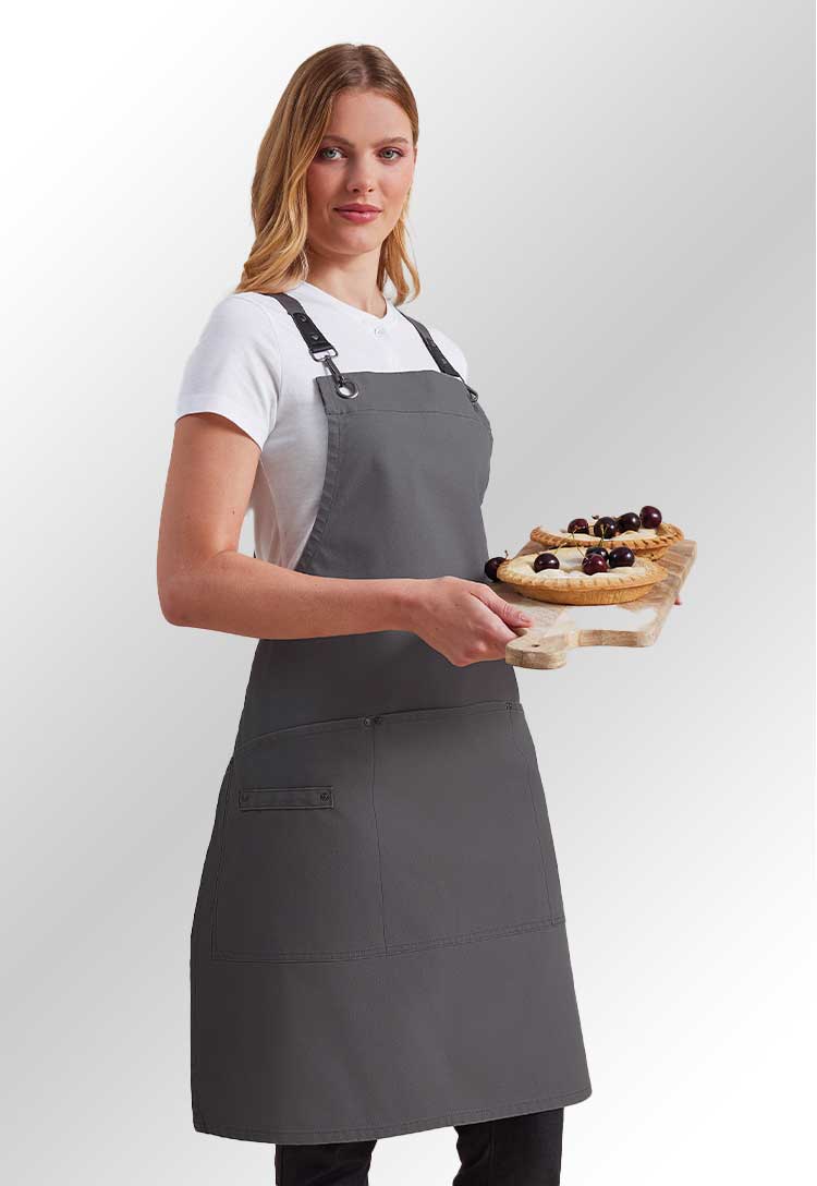 A model wearing a PR182 Clip ‘n’ Clasp cross-back bib apron in Dark Grey