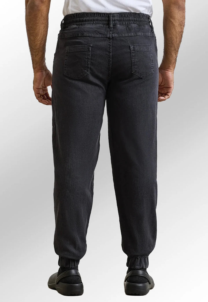 Rear view of model wearing the Premier Workwear Chef's Artisan Jogger Bottoms PR556 in Black Denim.