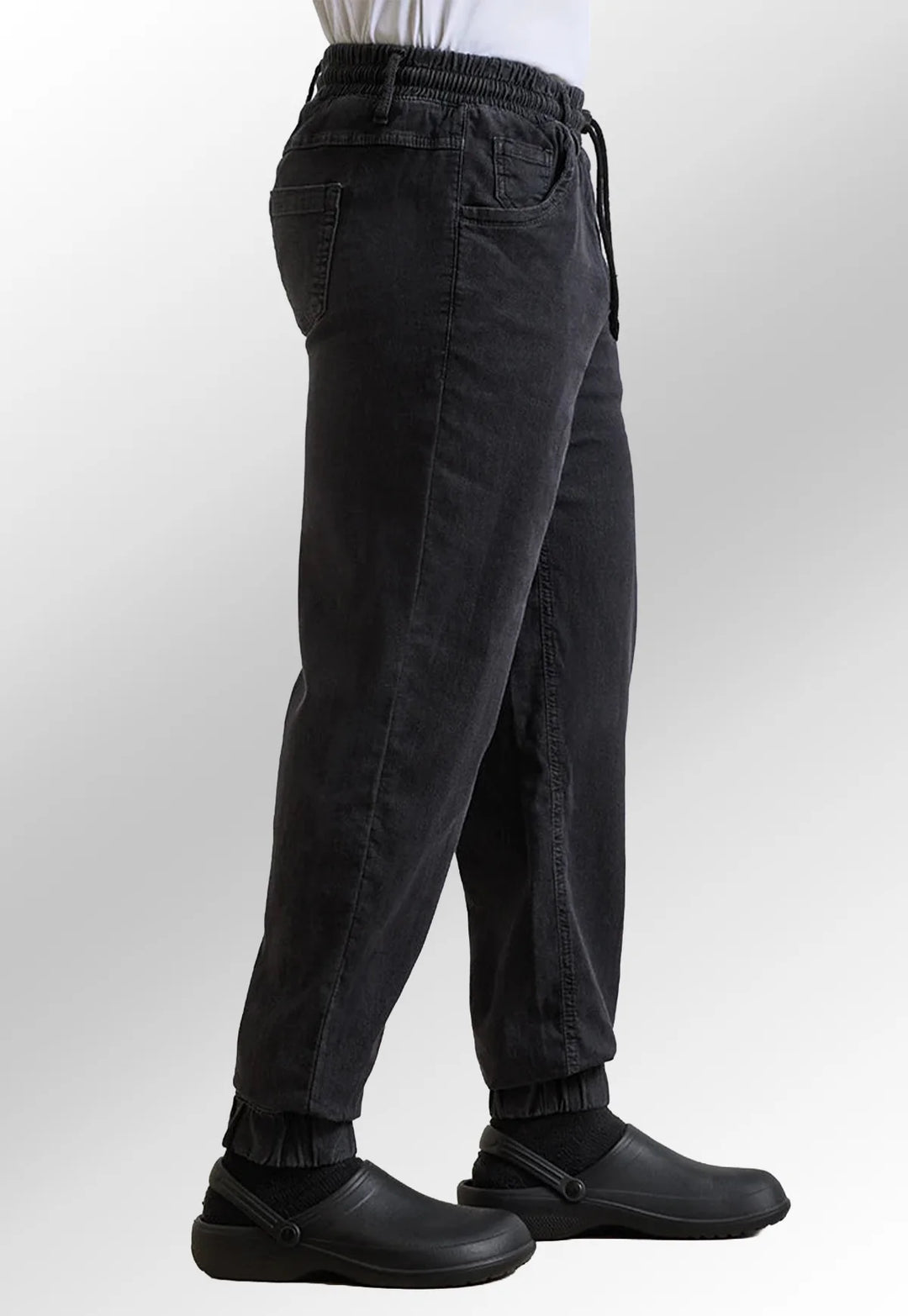 Side view of model wearing the Premier Workwear Chef's Artisan Jogger Bottoms PR556 in Black Denim.