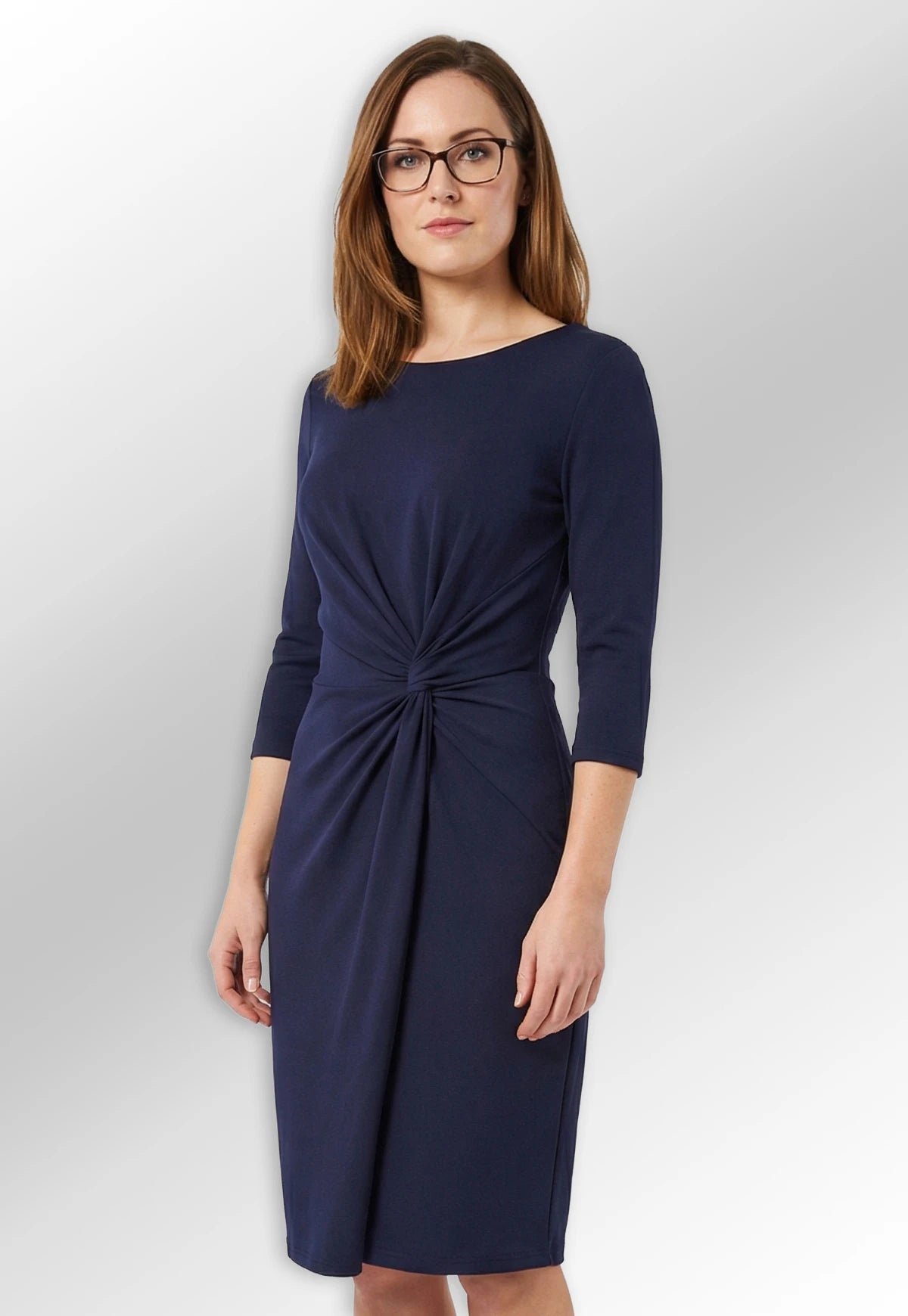 Woman wearing the navy blue Neptune dress with a front knot detail from the Brook Taverner Women's One Collection.